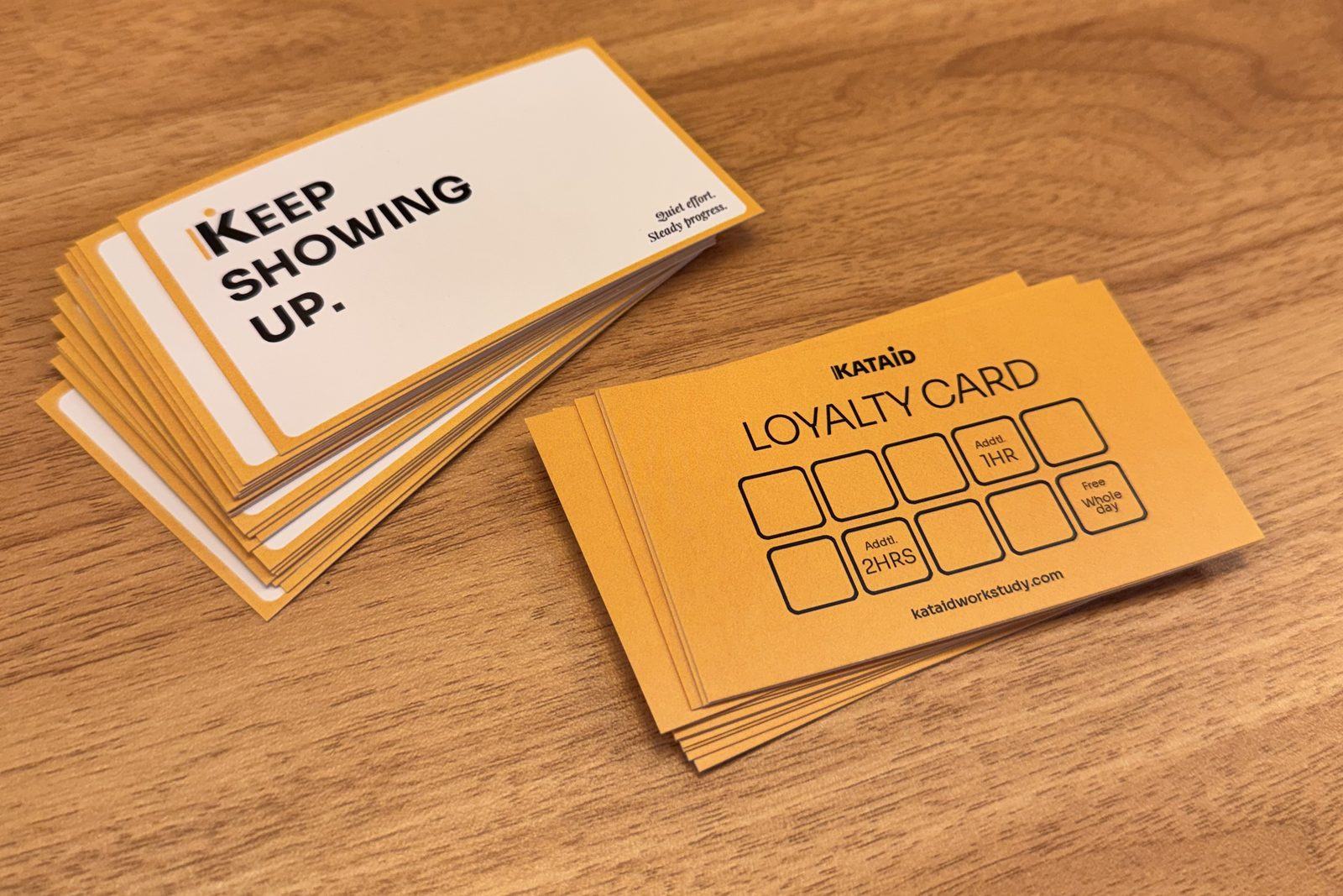A stack of Kataid loyalty cards on a wooden table — one side reads Keep showing up, the other has ten stamp squares.